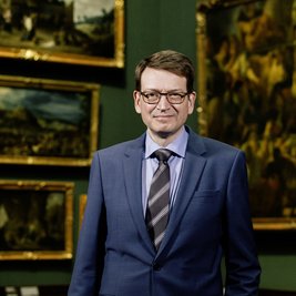 Mann im Anzug mit Gemälden im Hintergrund