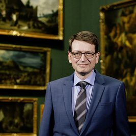 Mann im Anzug mit Gemälden im Hintergrund