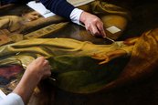 Detailaufnahme der Restaurierung der „Madonna des heiligen Sebastian“ zwei Hände arbeiten vorsichtig an liegendem Gemälde