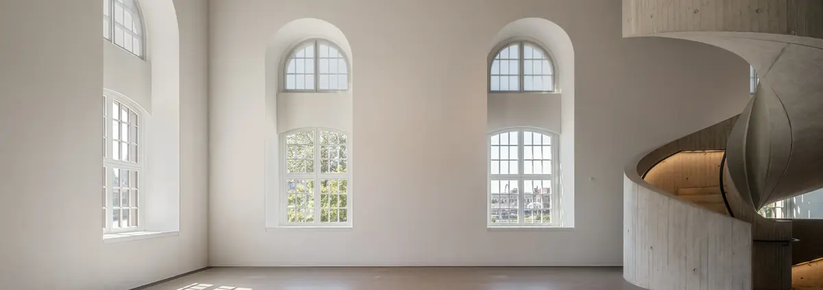 Ein lichtdurchfluteter Raum mit hohen Fenstern und einer geschwungenen Treppe.