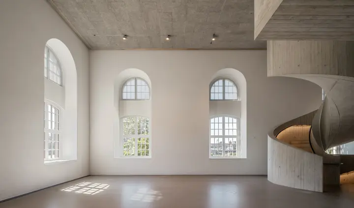 Ein lichtdurchfluteter Raum mit hohen Fenstern und einer geschwungenen Treppe.