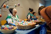 Volkskünstlerinnen zu Ostern im Jägerhof alte Frau in einer Tracht verkauft bemalte Ostereier an einem Tisch