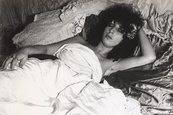 Colette a.k.a. Colette Lumiere: “‘Ancora tu’ – living in a space for six days with all my personal belongings”, Internationaler Kunstmarkt Köln, 1977 Frau liegt in einem Bett, vorne eine Champagnerflasche