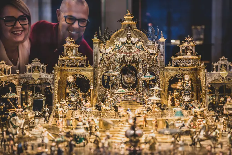 zwei Personen schauen auf eine goldene Miniaturszenerie