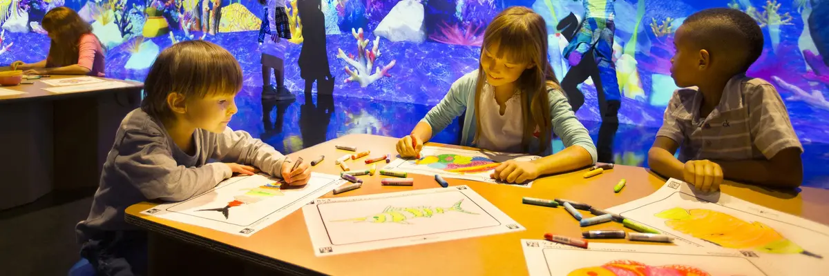 Drei Kinder zeichnen Fische vor einem digitalen Aquarium