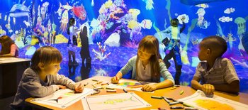 Drei Kinder zeichnen Fische vor einem digitalen Aquarium