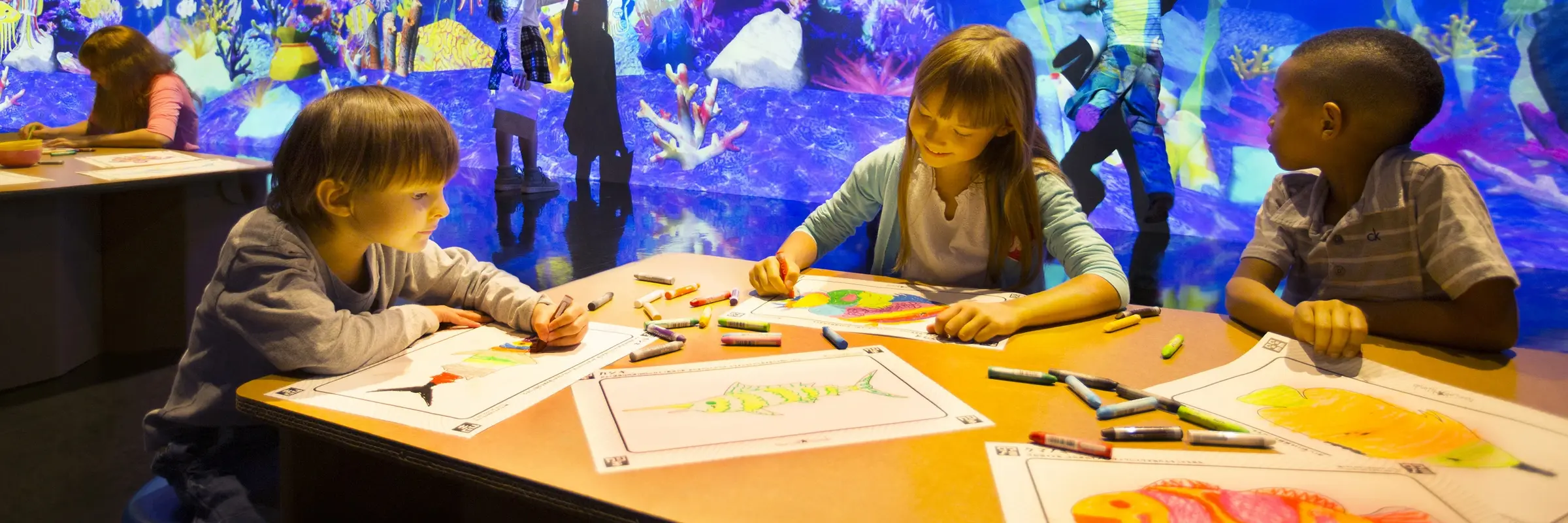 Drei Kinder zeichnen Fische vor einem digitalen Aquarium