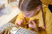 Klöppelschülerin der Volkskunstschule des Erzgebirgskreises Mädchen sitzt an einem Klöppelstück und macht eine Handarbeit