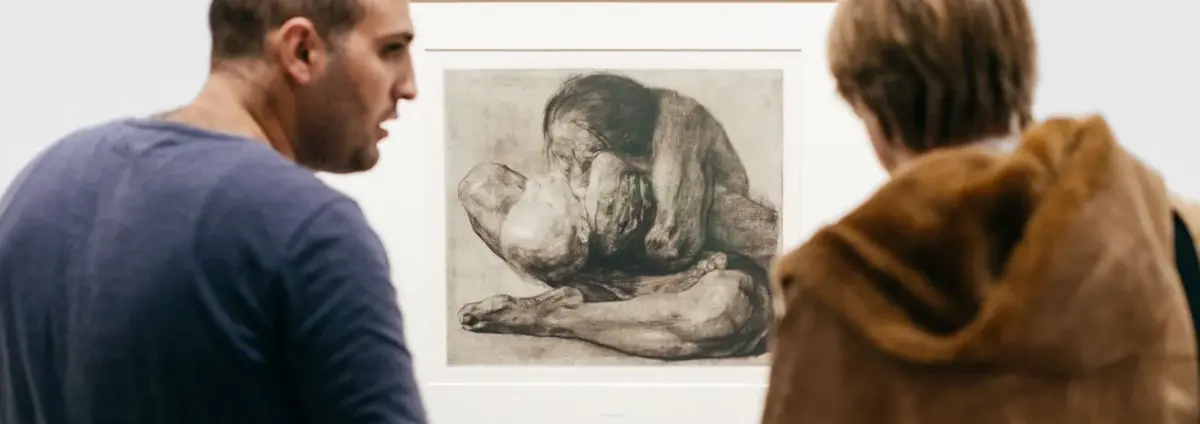 Zwei Besucher besprechen eine Druckgraphik von Käthe Kollwitz.
