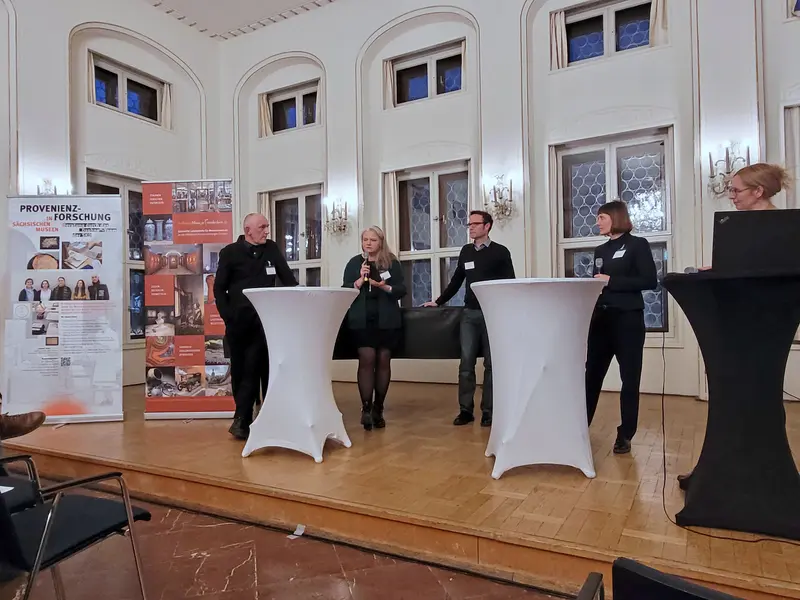 mehrere Personen auf einer Bühne an Stehtischen