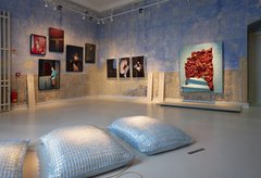 blauer Raum mit Fotografien an den Wänden und Kissen im Vordergrund