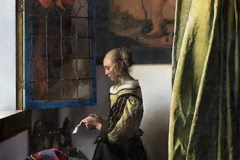 Eine Frau steht vor einem Fester und liest einen Brief