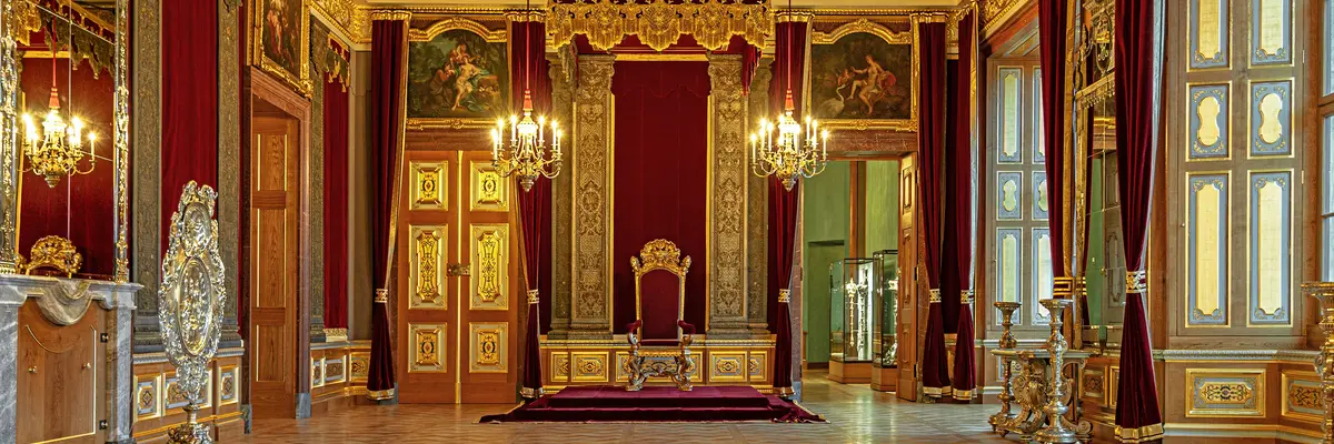 festlicher Raum mit prunkvollen goldenen Elementen und einem Thron