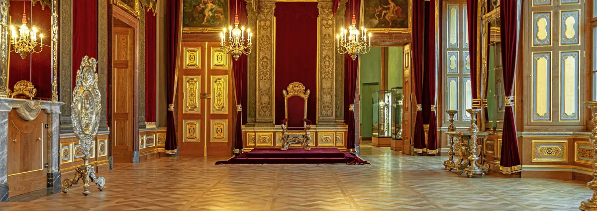 festlicher Raum mit prunkvollen goldenen Elementen und einem Thron