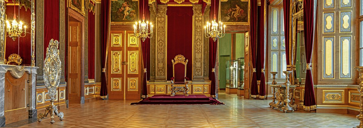 festlicher Raum mit prunkvollen goldenen Elementen und einem Thron