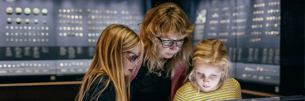 drei Besucher, darunter zwei Kinder, schauen sich Vitrine mit Münzen an