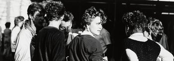 Schwarz-Weiß-Fotografie einer Gruppe, die mit den Rücken zum Betrachter steht, nur eine Frau blickt über die Schulter.
