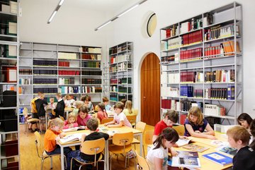 ein Raum mit Bücherregalen und Kindern an Tischen