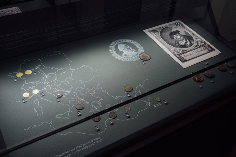 Vitrine mit Münzen, einer Zeichnung und einer Reisekarte
