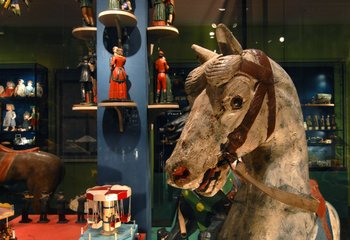 ein Karussell-Pferd, im Hintergrund kleine Figuren