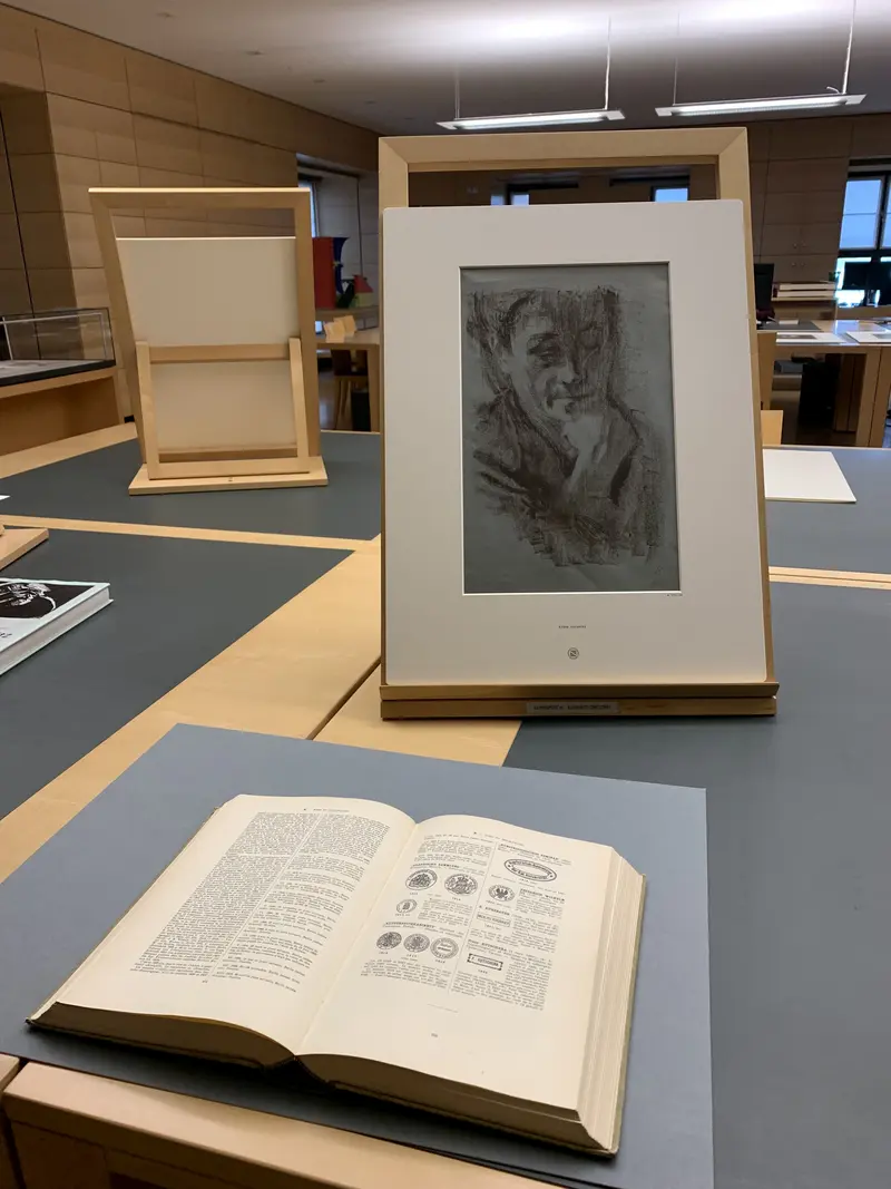 Auf einem Tisch liegt ein aufgeschlagenes Buch und eine Portätskizze