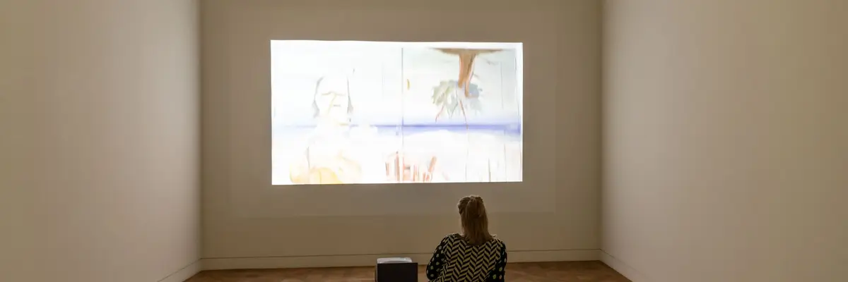 Projektion eines Filmes an eine Wand mit Frau davorsitzend