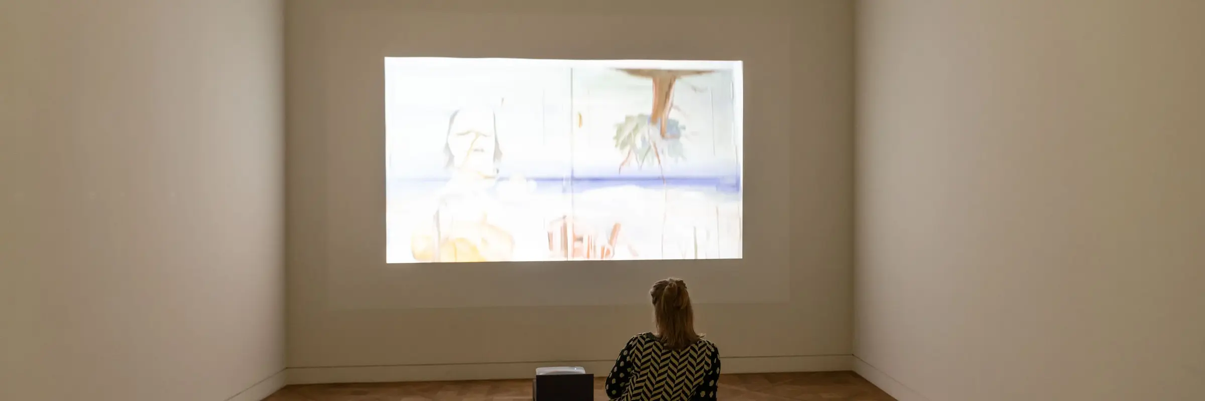 Projektion eines Filmes an eine Wand mit Frau davorsitzend