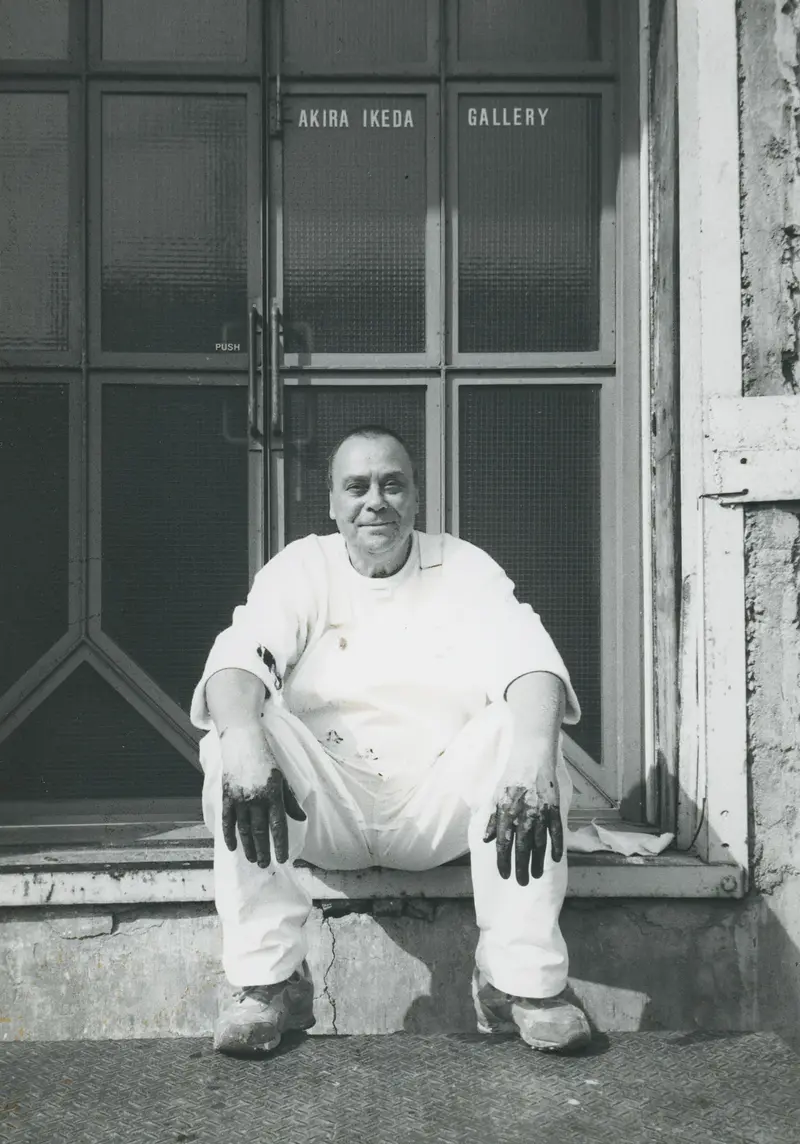 Schwarz-weißes Porträt von Günther Uecker, der auf einer Türschwelle sitzt