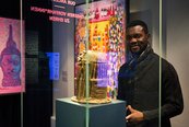 dunkelhäutiger Künstler steht hinter Glasvitrine, in der eine Benin-Bronze ist