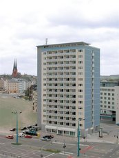 Ein Plattenbau, davor eine befahrene Straße