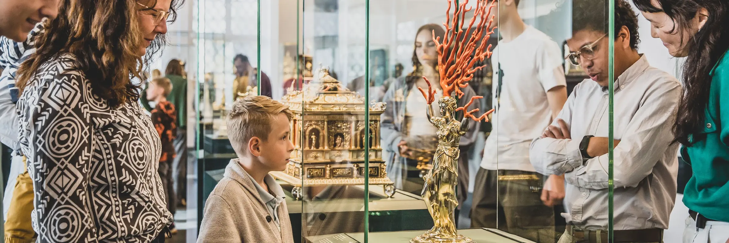 Besucher, die sich eine goldene Figur mit Korallen in einer Vitrine anschauen