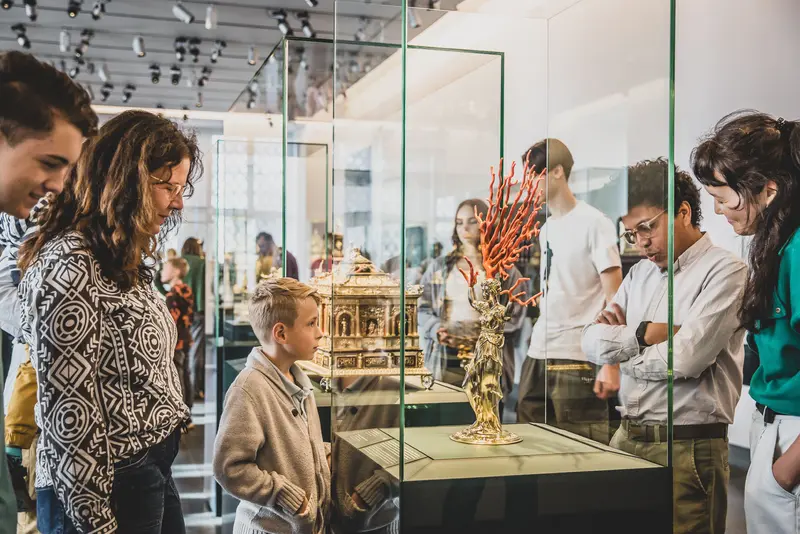 Besucher, die sich eine goldene Figur mit Korallen in einer Vitrine anschauen